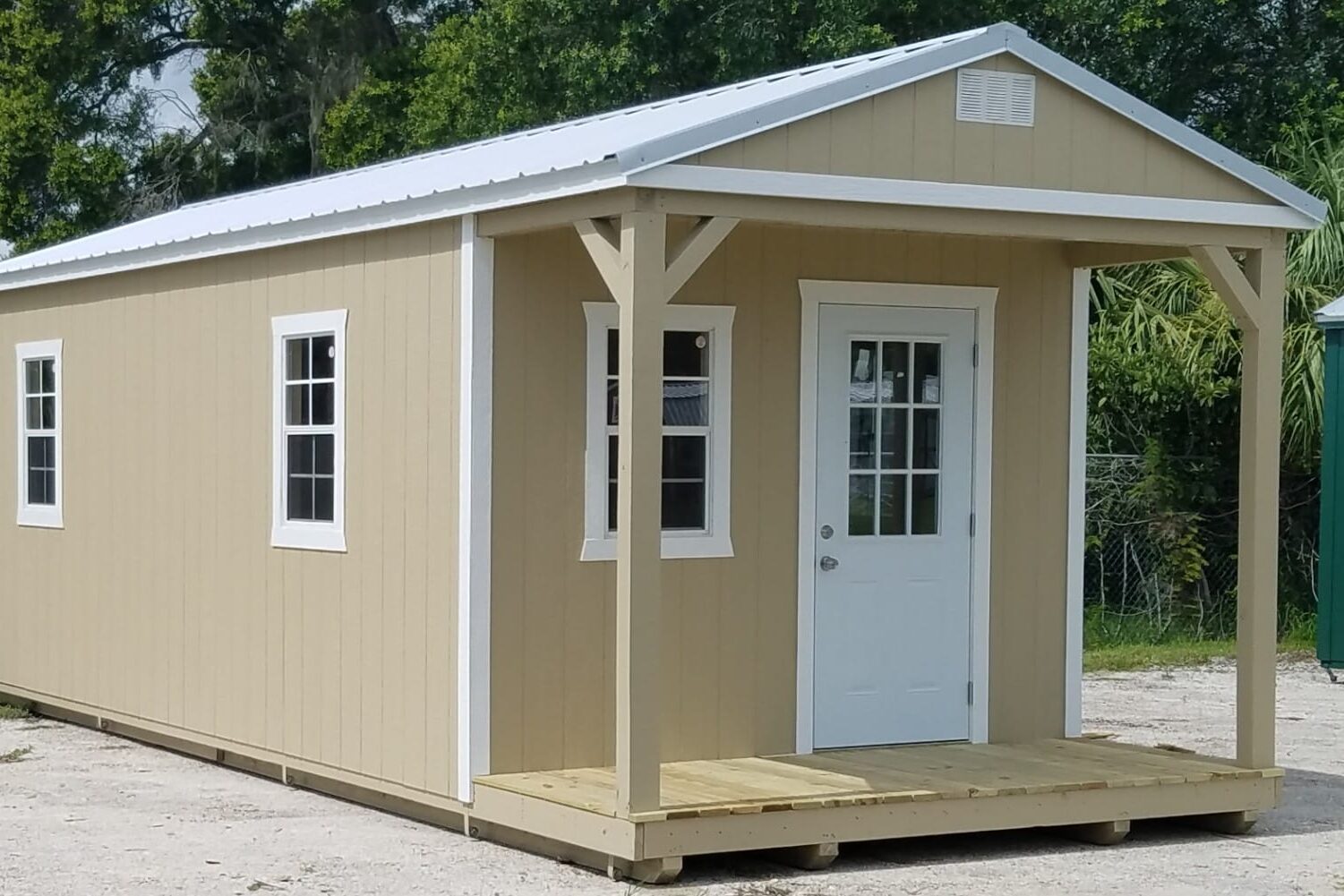 tan cabin with front porch and white trim as well as three windows and a white door